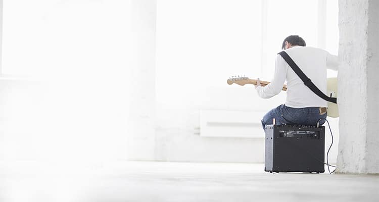 A man sitting on a guitar amp practising playing an electric guitar